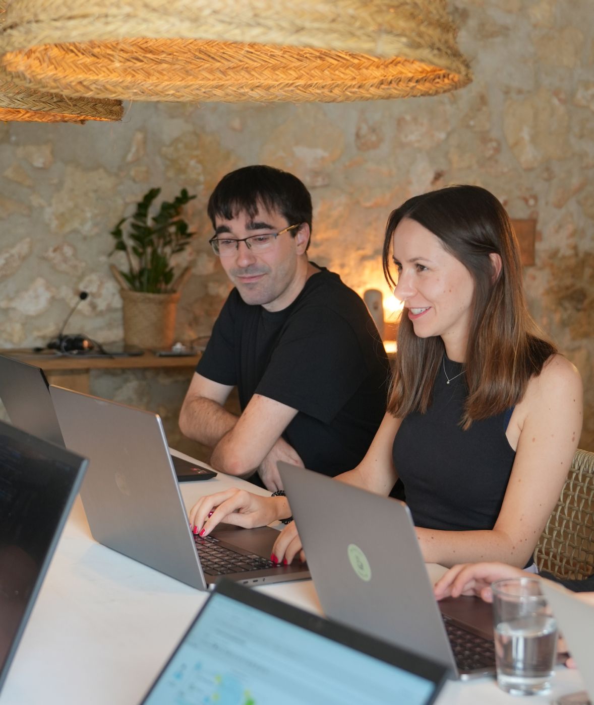 Zwei Teammitglieder einer Digitalagentur arbeiten lächelnd gemeinsam an Laptops in einem modernen Büro mit gemütlicher Atmosphäre.